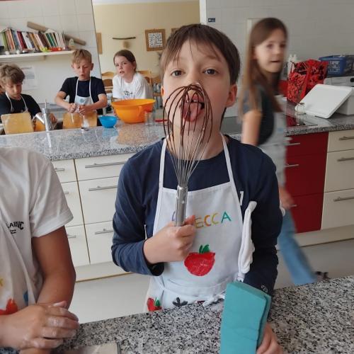 Kinder beim Kochen, Bub schleckt im Vordergrund Schneebesen ab