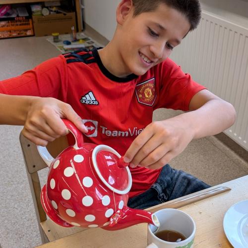 Junge schenkt Tee in eine Tasse ein