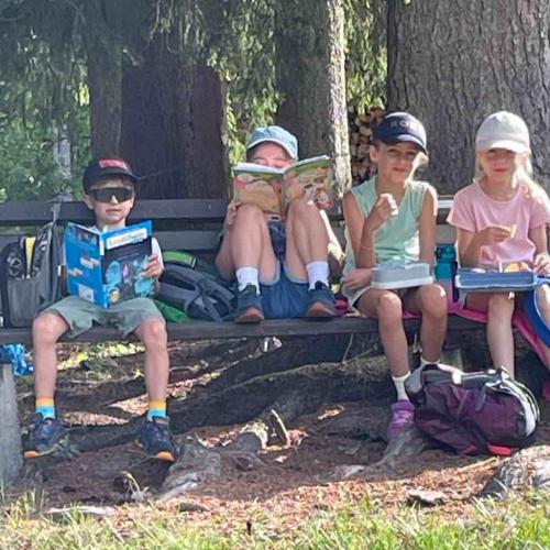 Kinder sitzen auf Bank unter Baum und lesen