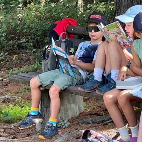 Kinder sitzen auf Bank unter Baum und lesen