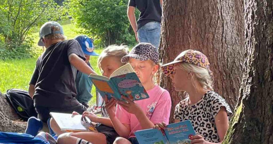 Kinder sitzen unter Baum und lesen